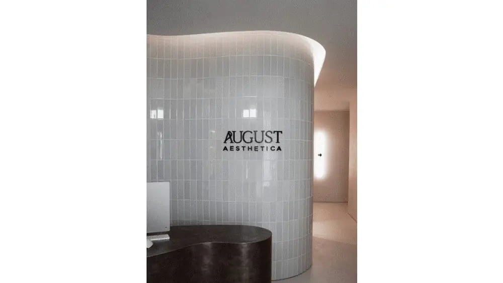 August Aesthetica reception with curved white tile wall and backlit logo